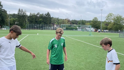 Drei Jungen spielen auf einem Kunstrasenplatz Fußball