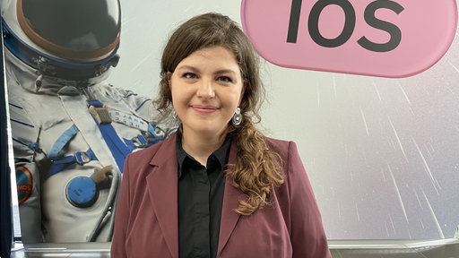 Eine Frau mit braunen Haaren schaut lächelnd in die Kamera.