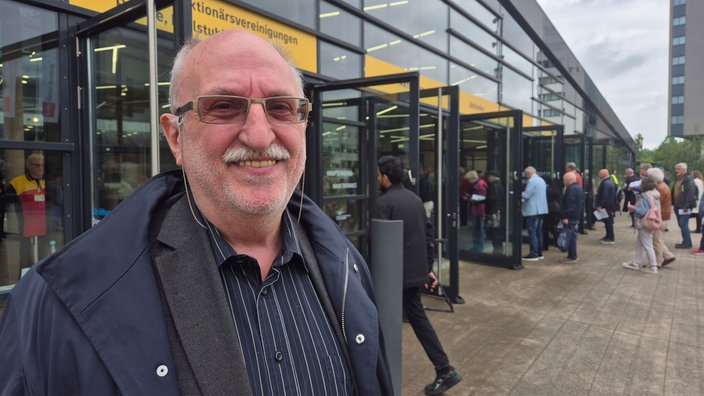 Ein Mann mit Brille steht vor dem DHL-Gebäude. Er lächelt in die Kamera.