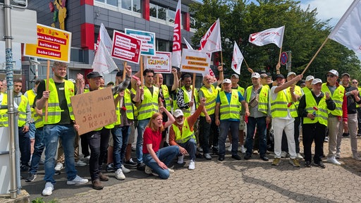 Mitarbeiter in Warnwesen und mit Plakaten und Fahnen in der Hand streiken.