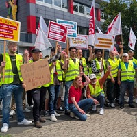 Mitarbeiter in Warnwesen und mit Plakaten und Fahnen in der Hand streiken.