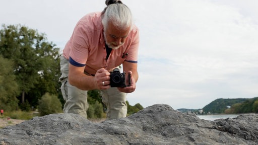Ein Mann mit rosa Oberteil bückt sich zum fotografieren