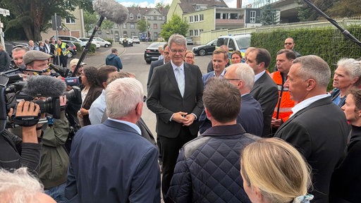 Ein großer Mann im Anzug mit grauen Haaren und einer Brille, Bundesverkehrsminister Patrick Schnieder, wird von einer Gruppe von Reportern interviewt.