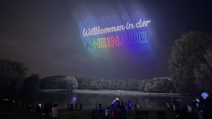 Drohnen formen die Worte "Wilkommen in der Rheinaue" über dem Himmel in der Rheinaue