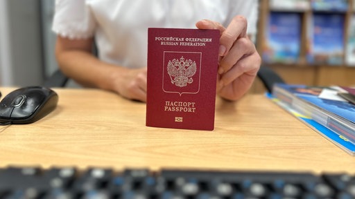 Ein russischer Reisepass auf einem Tisch. Eine Person hält diesen mit der Hand am oberen Rand fest.