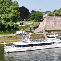 Ein weißes Schiff liegt an einem Flussufer an.