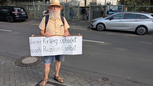Ein Mann steht mit einem Plakat vor dem russischen Konsulat in Bonn, mit der Aufschirft Der Krieg schadet auch Russland selbst...