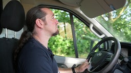 Ein Mann mit langem Zopf fährt ein Auto.