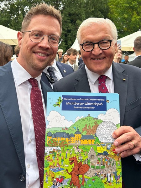 Der Bundespräsident hält das Wimmelbuch vor sich. Links daneben der Bürgermeister Swen Christian