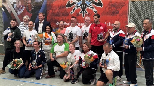 Gruppnebild mehrerer Personen mit Auszeichnungen und Blumenstäußen in der Hand