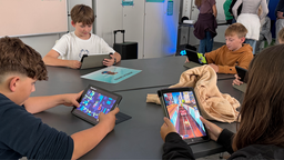 Fünf Schüler sitzen an einem Tisch und spielen jeweils an einem Tablet Videospiele