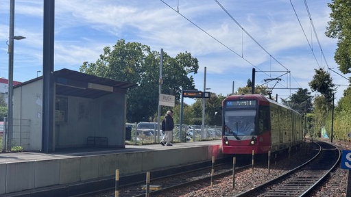 Bahn hält an einem Bahnsteig auf dem eine Person Richtung Bahn geht