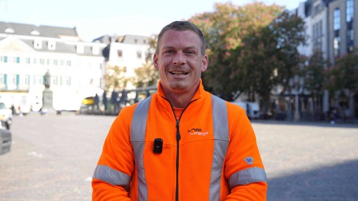 Ein Mann in orangener Arbeitskleidung lächelt in die Kamera