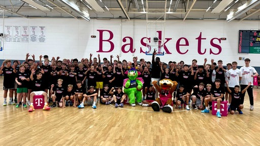 Gruppenfoto von ganz vielen Jugendlichen, einem Profi-Basketsballspieler und zwei Maskottchen