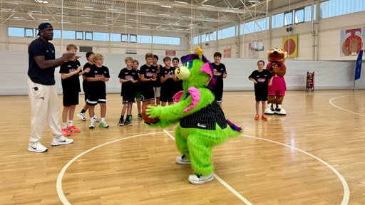 Jugendliche, ein großer Mann und ein Maskottchen spielen Basketball