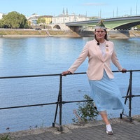 Frau in rosa Jackett und mit Karnevalsschiffchen auf dem Kopf lehnt an Geländer am Rhein