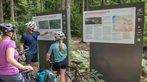 Eltern mit ihrem Kind lesen die auf dem Radweg aufgestellten Infotafeln