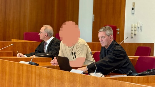 Mann mit gepixeltem Gesicht zwischen zwei Männern in dunkler Robe