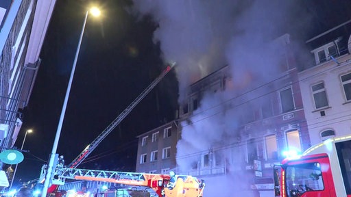 Feuerwehrleute versuchen nachts ein Haus zu löschen. Aus einem Fenster quillt dichter Rauch. 