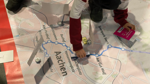 Auf dem Bild schiebt ein Kind ein Straßenbahnmodell über eine Karte der geplanten Tram-Strecke