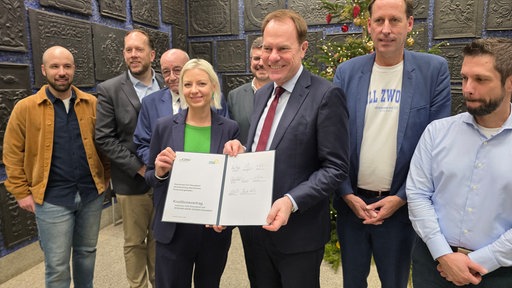 Mehrere Menschen stehen zusammen und halten ein unterschriebenes Papier vor sich