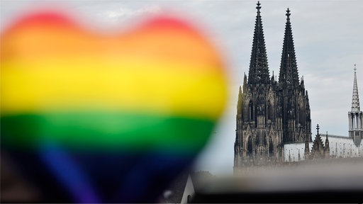 Symbolbild: Regenbogenfarbenes Herz im Vordergrund, Kölner Dom im Hintergrund