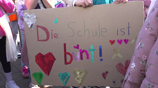 Kinder halten ein buntes Plakat mit der Aufschrift "Die Schule ist bunt" in den Händen