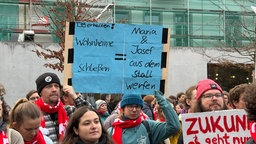 Demonstrierende hält ein blaues Plakat hoch