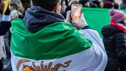 Mann in Iranische Flagge gewickelt, hält sein Handy hoch um die Demonstration zu filmen