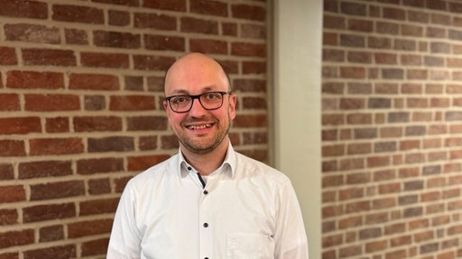 Porträtaufnahme;: Tobias Wiegelmann im weißen Hemd vor einer Klinkerwand