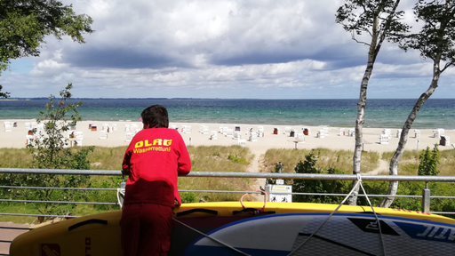 Ein Mann der DLRG schaut auf den Strand der Ostsee.