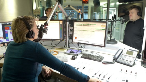 Im Radiostudio sitzt die Moderatorin und im Hintergrund steht der Druckluft Sänger am Mikrophon.