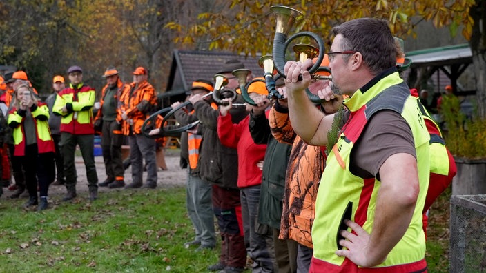 Mehrere Jäger stehen versammelt und spielen das Horn.