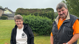 Ein Mann und eine Frau stehen in einem Garten. Die beiden schauen lächelnd in die Kamera.