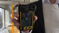 Ein Mann hält eine Bodycam in der Hand.