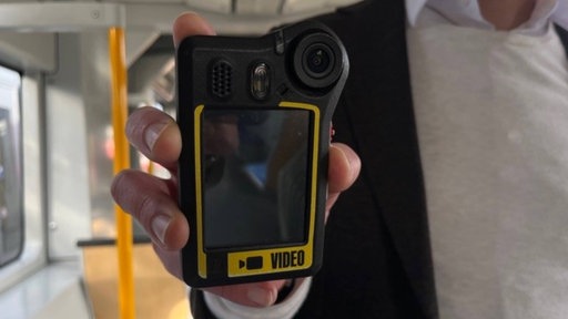 Ein Mann hält eine Bodycam in der Hand.