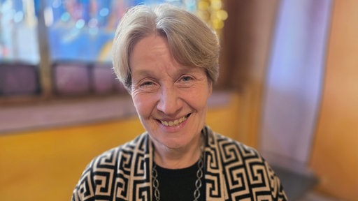Eine Frau lächelt in die Kamera, im Hintergrund sieht man gelbe Wände