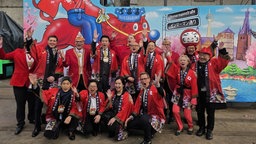 Die Verantwortlichen des ersten japanischen Karnevalswagens für den Düsseldorfer Rosenmontagszug stehen für ein Gruppenbild vor dem bunten Wagen.