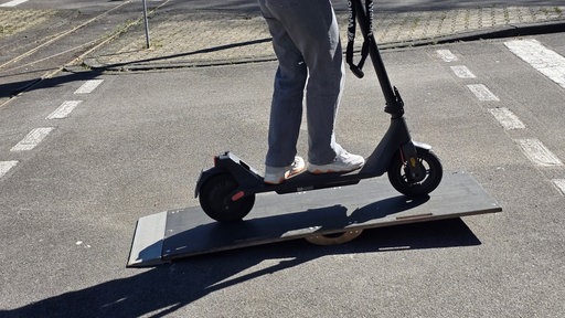Jugendliche auf E-Scooter fährt kleine Rampe hoch.