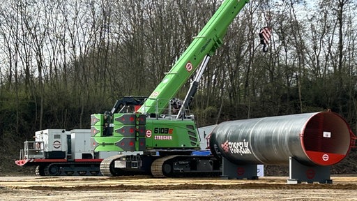 Ein grüner Bagger steht vor einer großen Röhre, die verlegt werden soll.