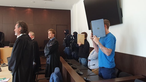 Zwei Männer stehend halten Mappen vor ihr Gesicht