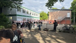 Mehrere Schüler halten ein "Herzlich Willkommen" Banner hoch und begrüßen die gerade angekommenen Schüler. 