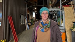 Eine Frau mit blauer Strickmütze steht in einer Landwirtschaftlichen Halle, im Hintergrund steht ein Traktor.