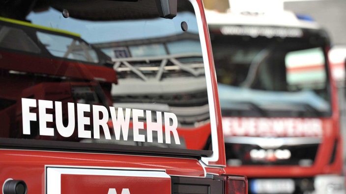 Symbolbild: Rotes Feuerwehrauto von vorne, im Hintergrund ein zweiter unscharfer Wagen