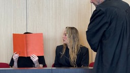 Der mutmaßlicher Fluchtwagenfahrer hält sich eine Kladde vor das Gesicht, neben ihm sitzt eine Dolmetscherin und vor ihm steht sein Verteidiger.