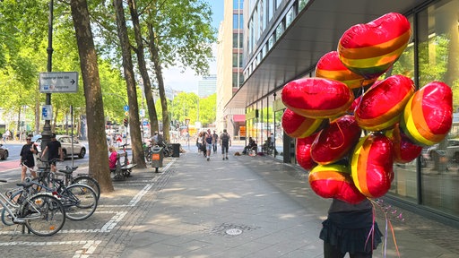 Eine Person geht mit vielen bunten Regenbogen-Ballons über den Gehweg.