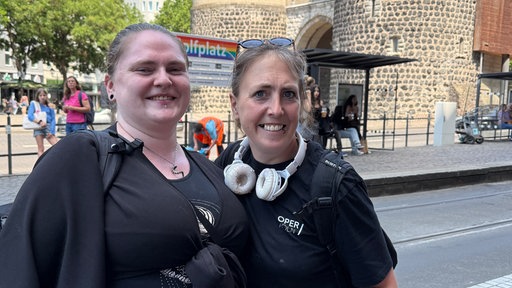 Im Bild stehen Jacky und Jenny nebeneinander vor der Haltestelle "Rudolfplatz".