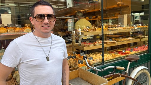 Olaf steht vor einer Bäckerei in der Kölner Ehrenstraße.
