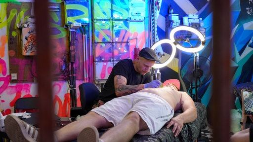 Ein Tätowierer tätowiert bei Parookaville 2025 einem Mann etwas auf die Brust.