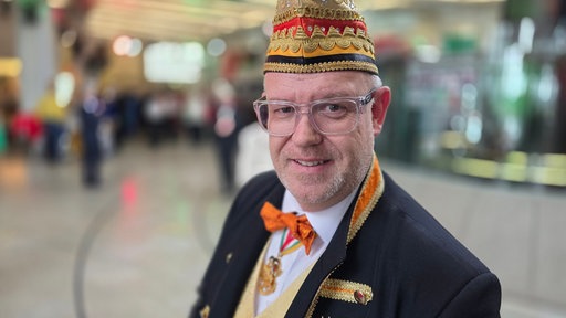 Ein Mann mit Dreitagebart, goldener Narrenkappe und durchsichtiger Brille im Landtag
